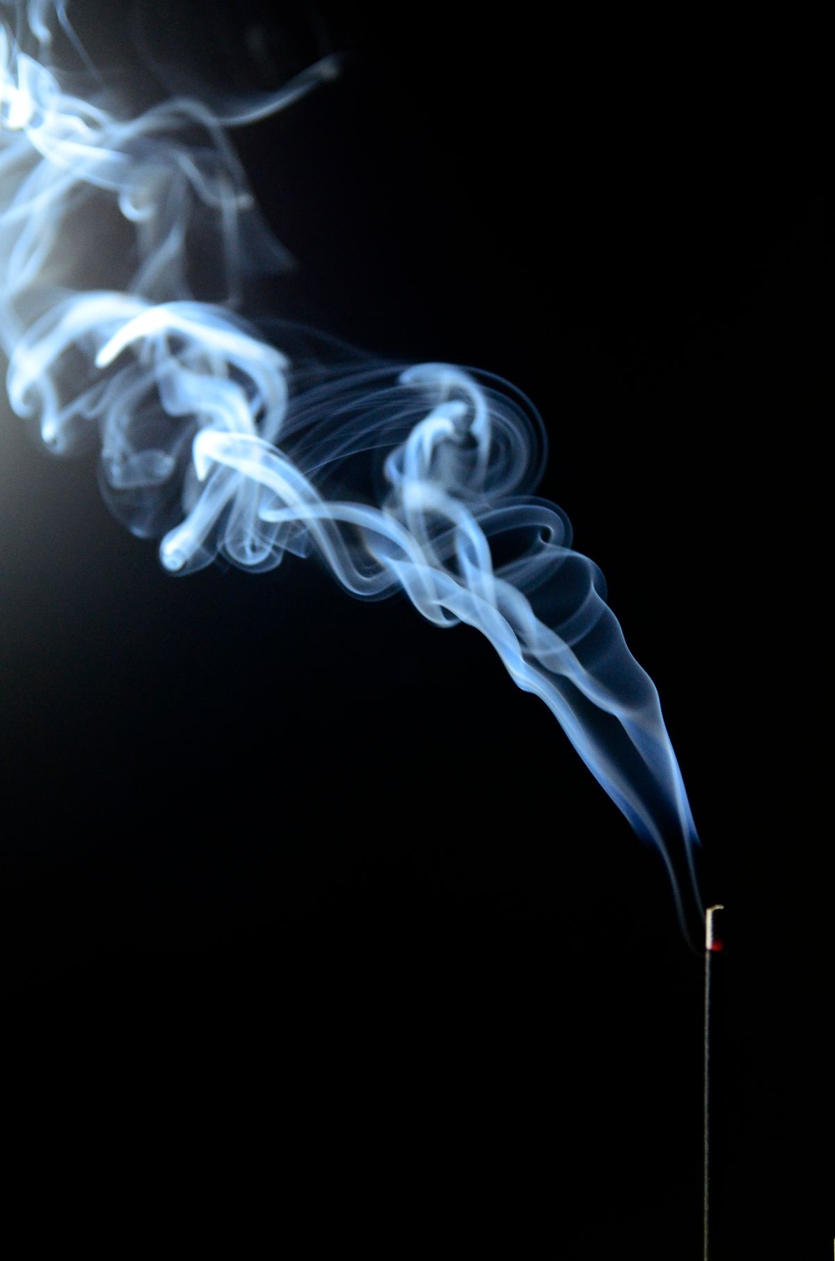Volutes de fumée d'encens s'élevant sur fond sombre, évocation de la capnomancie