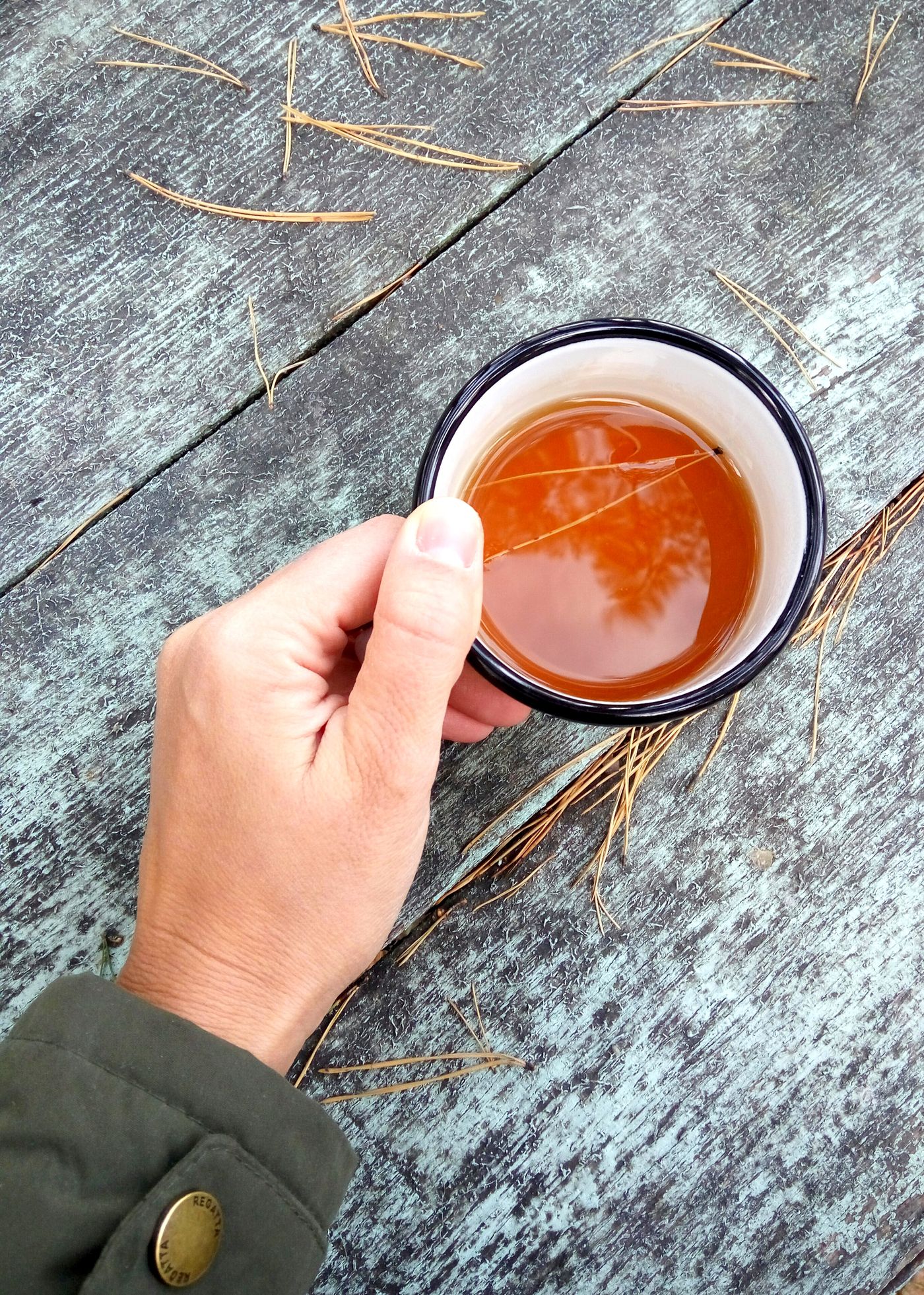 Main tenant une tasse de thé sur une table en bois, évocation de la tasséomancie