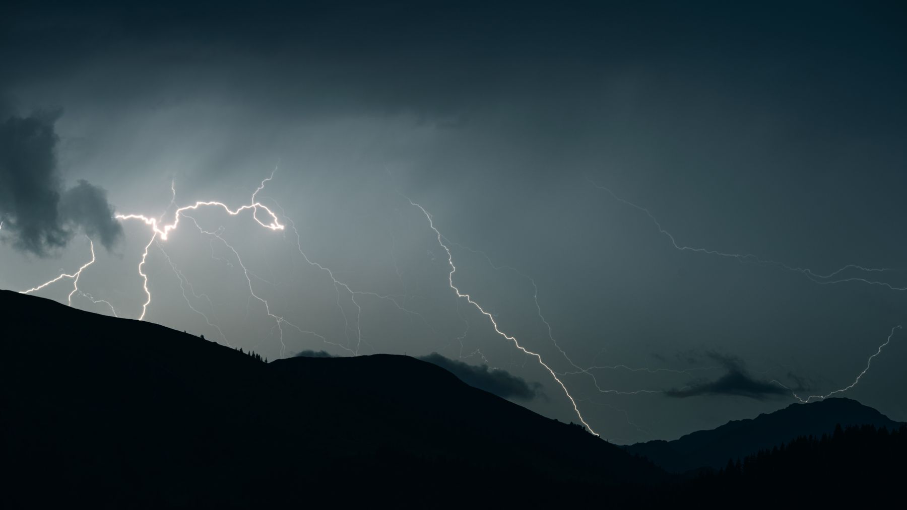 Éclair zébrant un ciel d'orage nocturne au-dessus de silhouettes de montagnes, évocation de la brontoscopie, la divination par le tonnerre